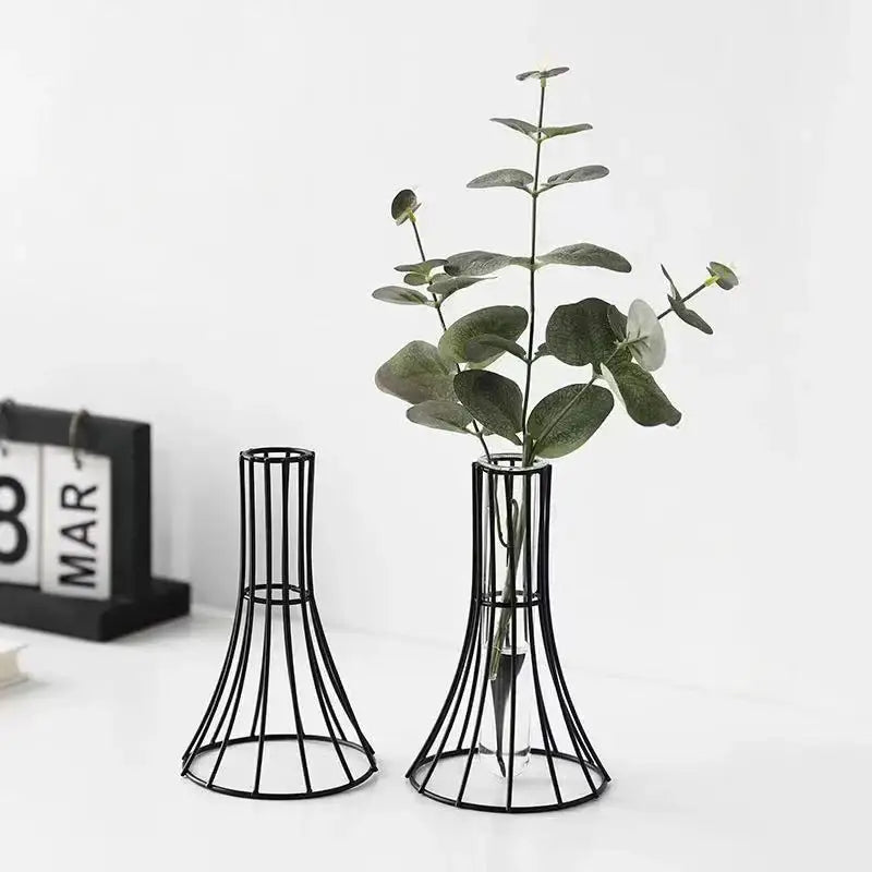 Black metal wireframe vase with flared base holding green eucalyptus branches for modern desk and metal flowers decor