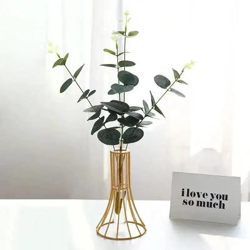 Gold wireframe vase holding dark green eucalyptus branches with small white flowers as modern desk decoration with metal flowers