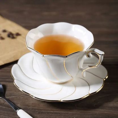 White bone china cup set with gold wave trim and scalloped edges filled with amber tea by decorbites gold wave