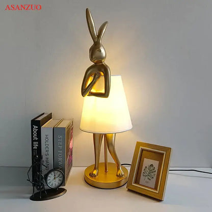 Golden bathing rabbit resin table lamp with sleek metallic finish and soft white fabric shade for bedroom decorbites decor