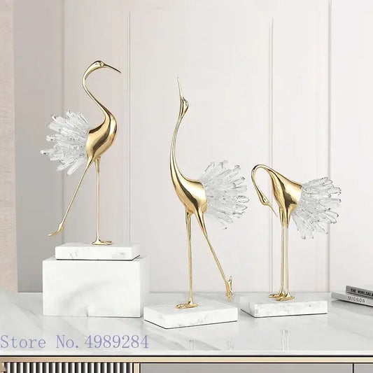 Three elegant gold-colored golden bird agate crane statues with crystal feathers on white bird agate marble bases for home decor