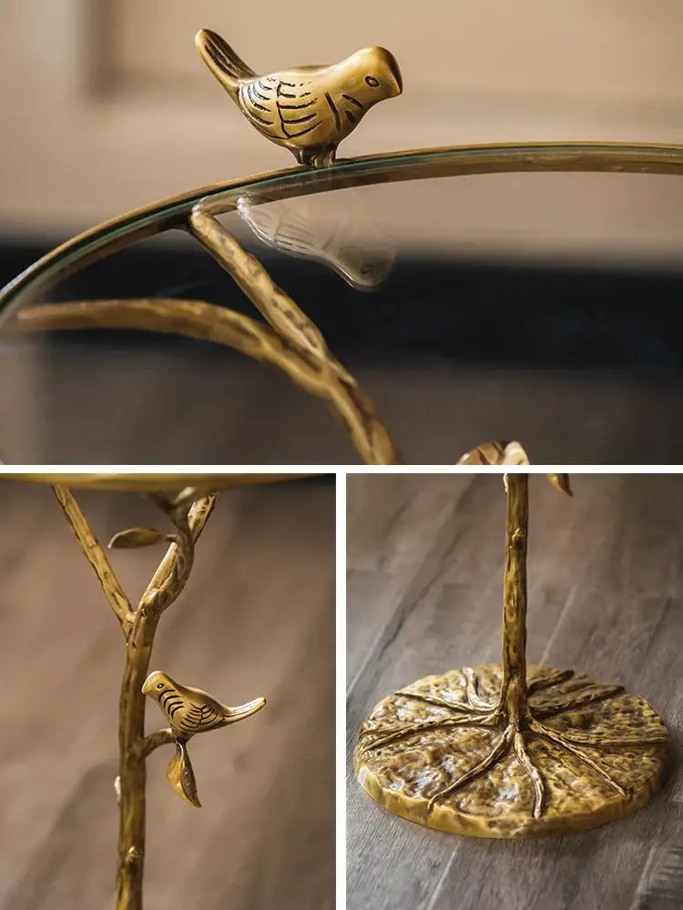 Golden brass bird figurine perched atop glass-topped decorbites brass bird tree side table with leaf-patterned base