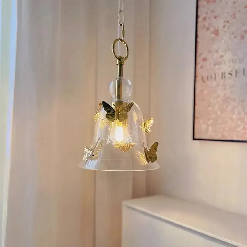 A glass pendant lamp with a delicate bell-shaped clear shade and golden butterfly details on a brass chain