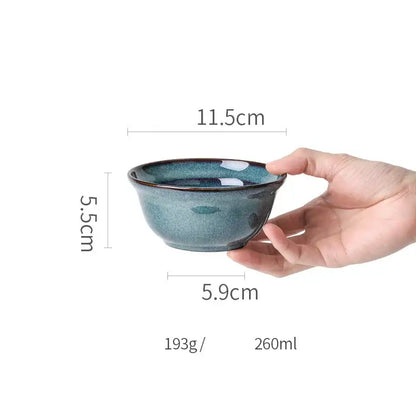 A hand holds a beautiful blue ceramic bowl with deep teal glaze and gold rim dinnerware dish for dining room use