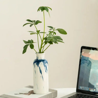 A white ceramic vase with blue splatter design holds a green plant for decorbites graffiti ceramic living room decor