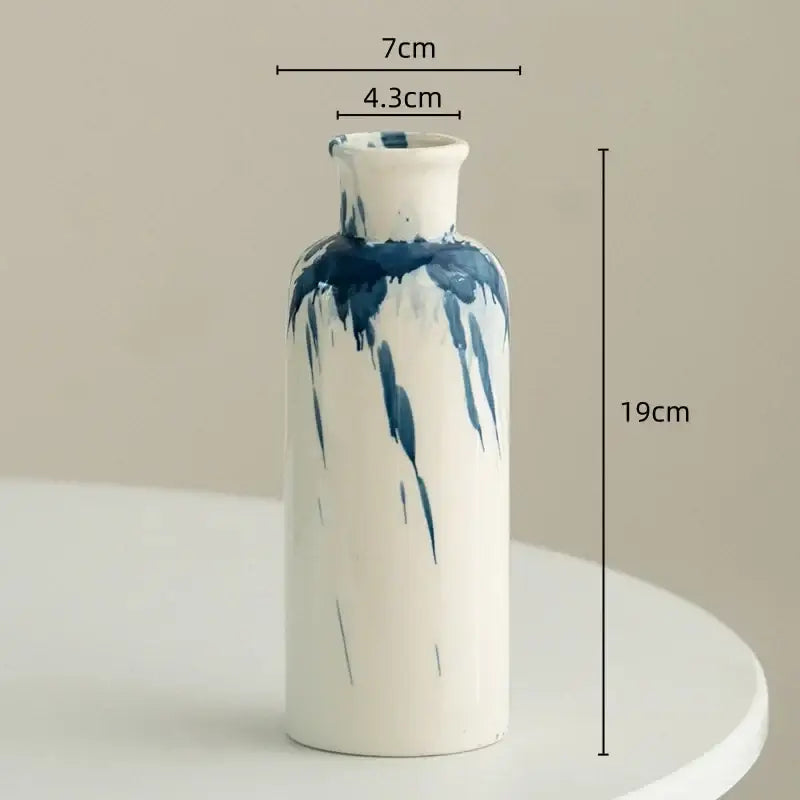 A slender white ceramic vase with blue hand-painted drip design for decorbites graffiti ceramic living room decor