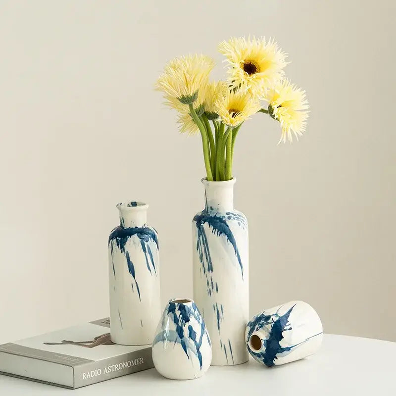 White ceramic graffiti ceramic vase with blue splatter design holding yellow flowers for living room decor