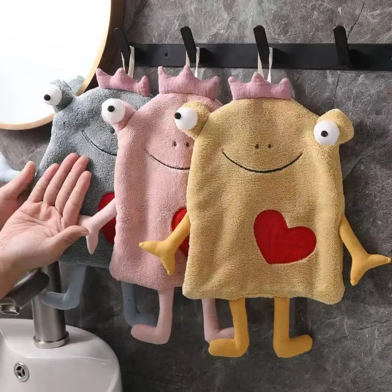 Three plush hand towels in gray, pink, and yellow with embroidered hearts and decorbites frog design hanging in bathroom decor