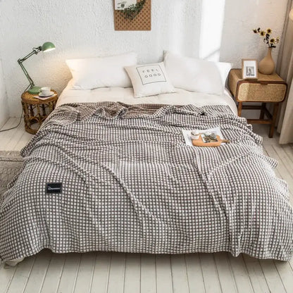 A cozy gray plaid coral fleece bed blanket with a soft checkered weave draped over a bedroom bedspread