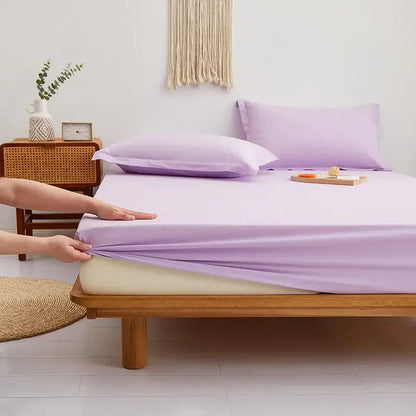 Lavender-colored smooth-textured decorbites cotton fitted sheet being stretched over a mattress in a gray decorbites sheet set