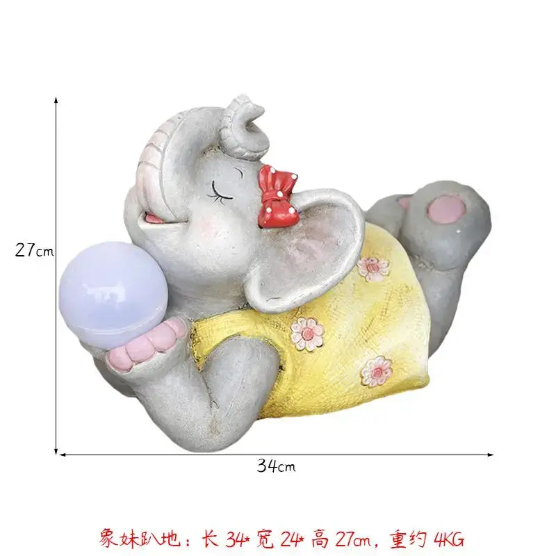 Gray ceramic elephant garden decoration wearing yellow floral dress holding blue orb with red bow on ear