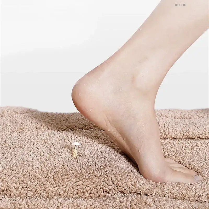 A delicate gold-toned foot-shaped charm with white accent rests on a gray decorbites geometric flocked bath mat