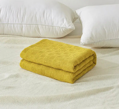 A neatly folded mustard yellow woven cotton waffle towel quilt with diamond texture for bedroom or office decorbites cotton waffle