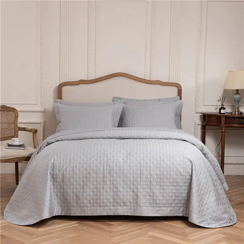 Light gray textured egyptian cotton quilt set with subtle pattern draped over wooden headboard in elegant bedroom