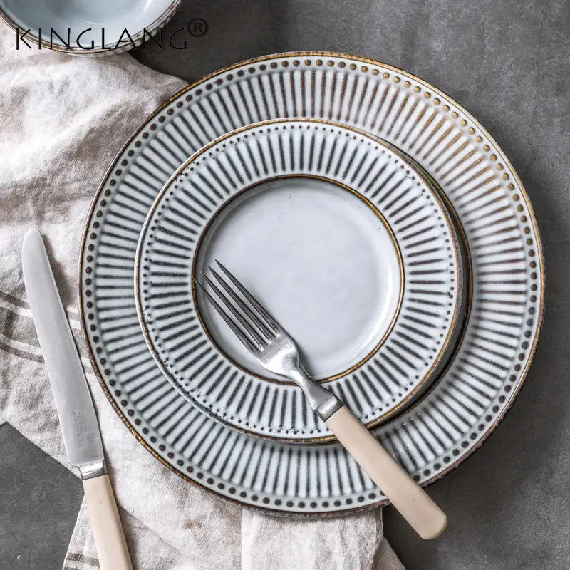Set of three stacked matte white ceramic plates with gold-toned rims from the gray and white striped ceramic wedding tableware set