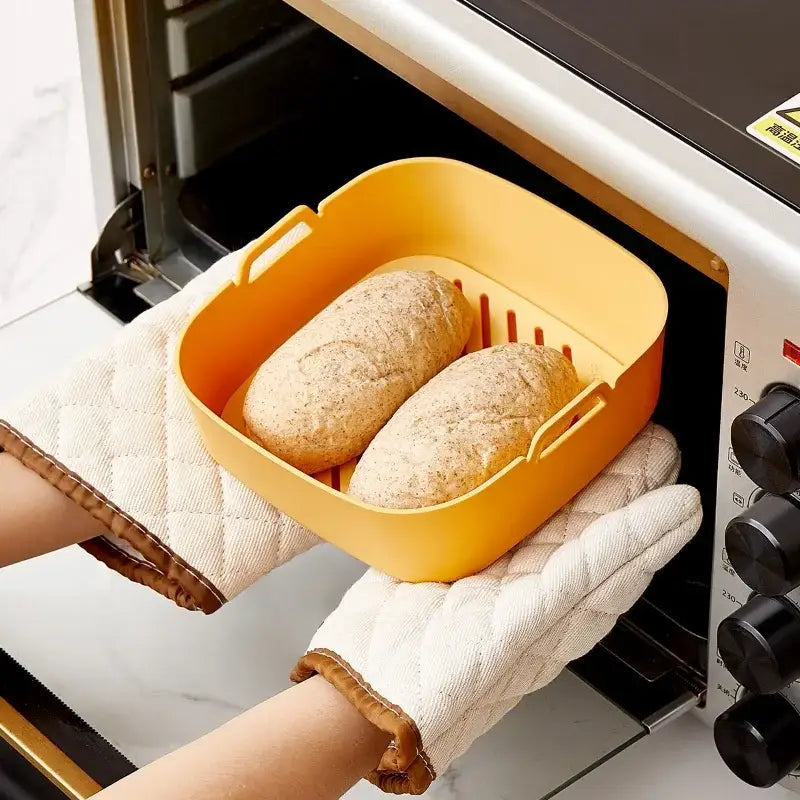 Yellow rectangular baking tray with handles and slotted base holding bread loaves for green and black silicone air fryer pot baking tray