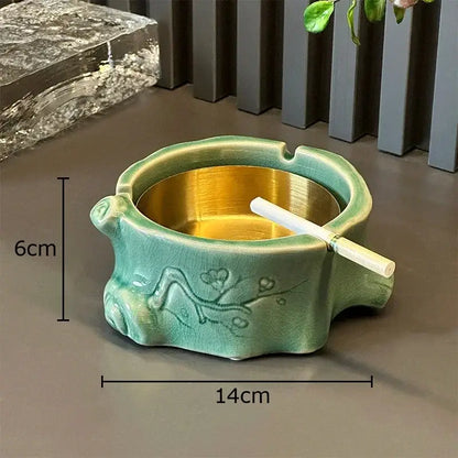 Teal ceramic ashtray with gold interior and floral relief alongside green ceramic bamboo tissue box for living room decor