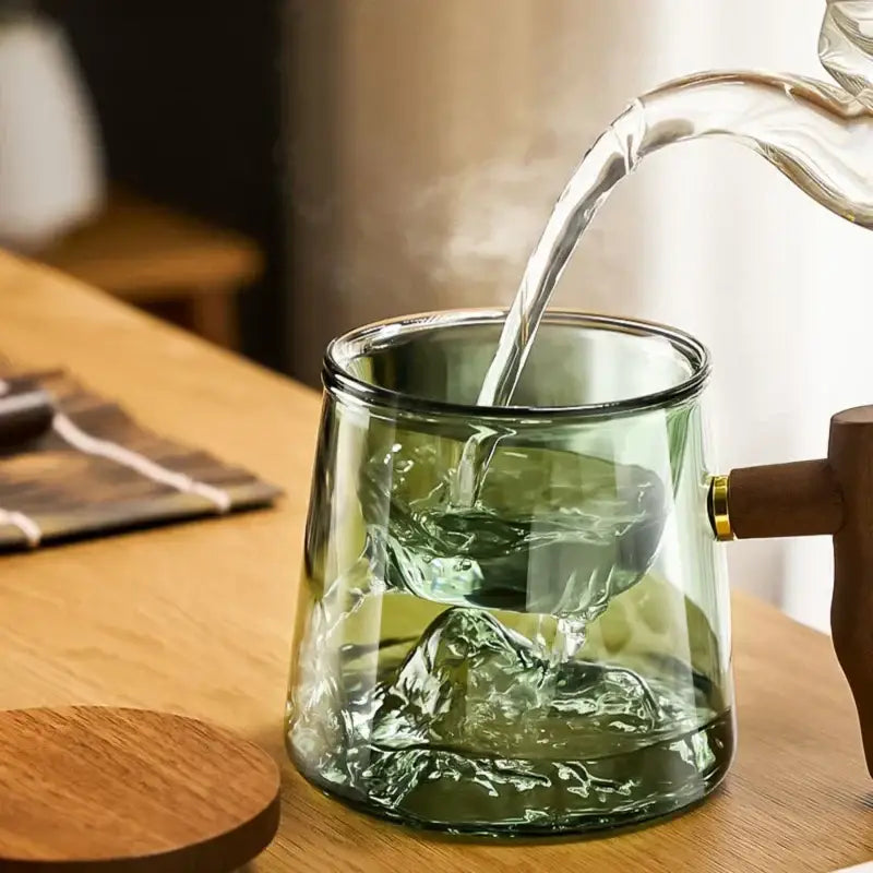 A translucent green glass tea cup set with wooden handle and gold accent pouring steaming water for decorbites glass tea