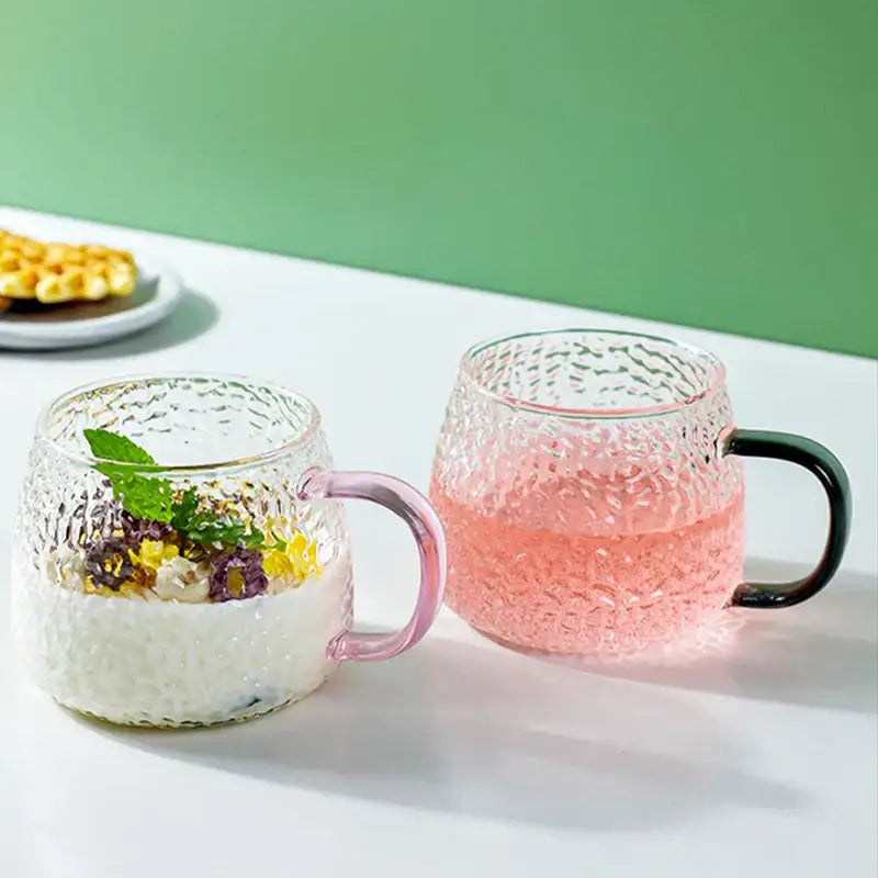 Two 400ml hammer pattern glass mugs with pink and black textured handles filled with colorful beverages