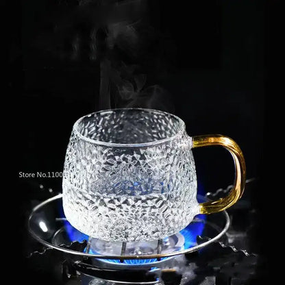 Hammered clear glass water cup with gold handle and textured pattern on matching saucer over a lit burner