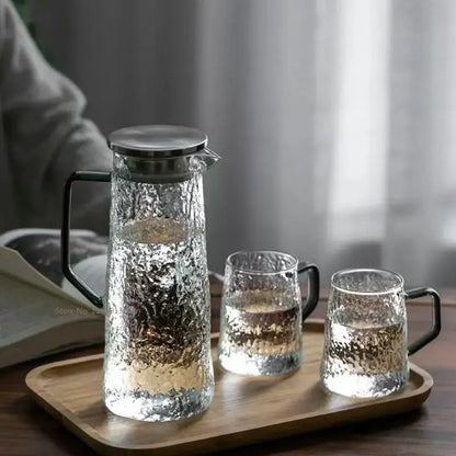 Clear hammered glass water pitcher with black handle and stainless steel lid paired with two textured glasses for decorbites gray amber water