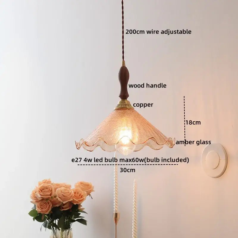 A warm amber glass pendant lamp with wooden handle and copper accents featuring an elegant scalloped design