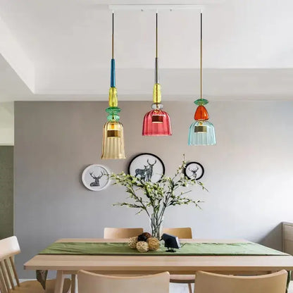 Three colorful hand-blown decorbites candy glass pendant lights with gold accents hang above a dining table