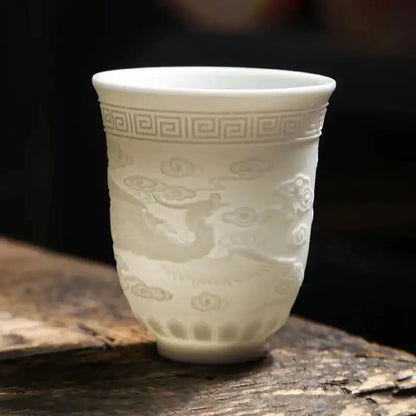 Delicate translucent white jade tea cup set with embossed cloud and dragon designs and greek key pattern near rim