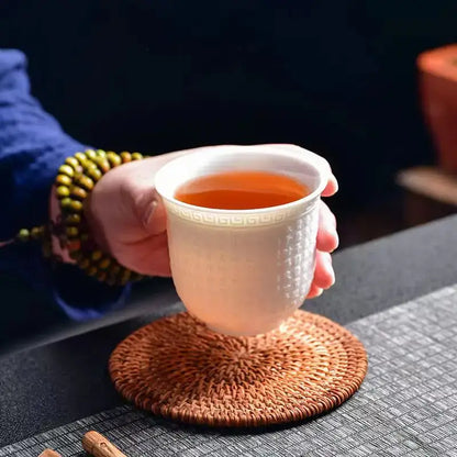 A white ceramic tea cup with geometric pattern and textured body filled with amber tea from a jade cup set
