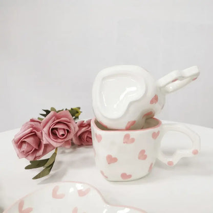 White ceramic love mug set with hand painted heart handles and pink polka dot design stacked in kitchen saucer set