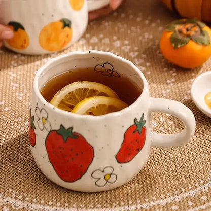 White ceramic cartoon fruit ceramic mug with hand-painted red strawberries and flowers filled with tea and lemon slices