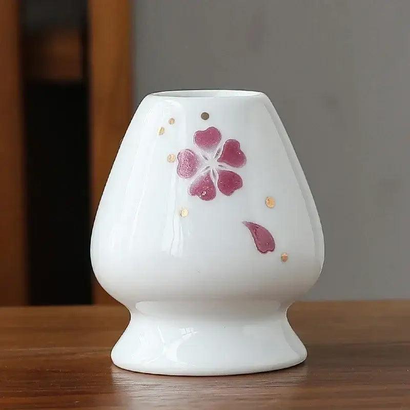 White ceramic matcha whisk holder stand with flared top, pink cherry blossom motifs, and gold dot accents