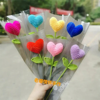 A hand woven love heart yarn crochet flower bouquet with vibrant pink blue yellow red and purple heart-shaped flowers