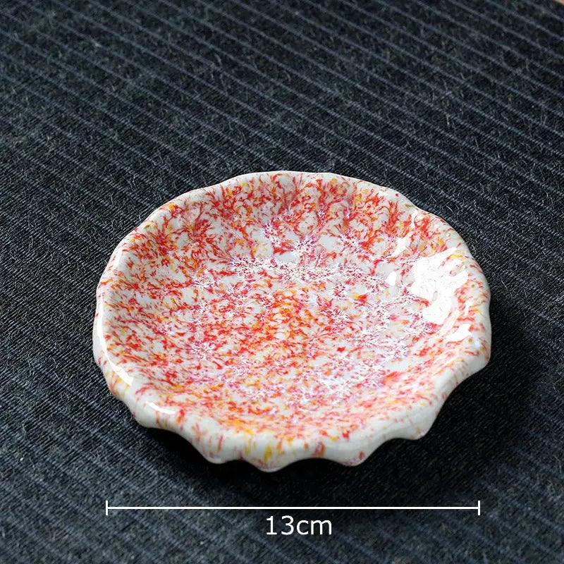A delicate white ceramic dish with scalloped edge and vibrant red orange speckles complements hammer pattern porcelain mugs