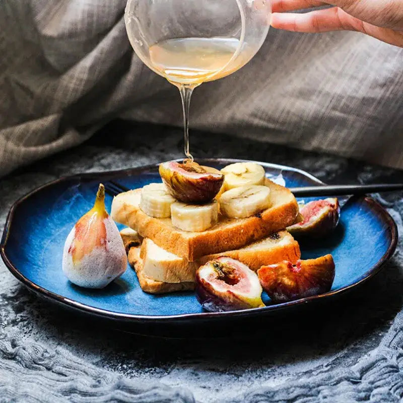 A handcrafted deep blue ceramic dessert plate from decorbites holds toasted bread with banana fig and honey topping