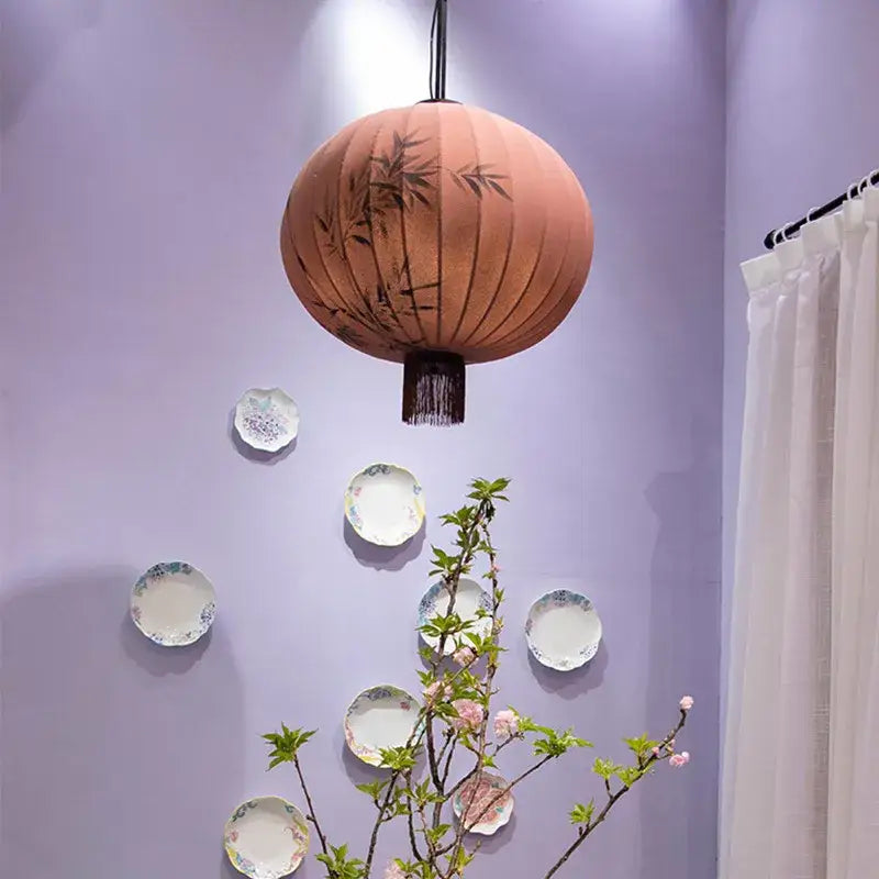 A peach and cream handmade decorbites bamboo lantern pendant with black bamboo leaf designs and dark fringe for dining room light