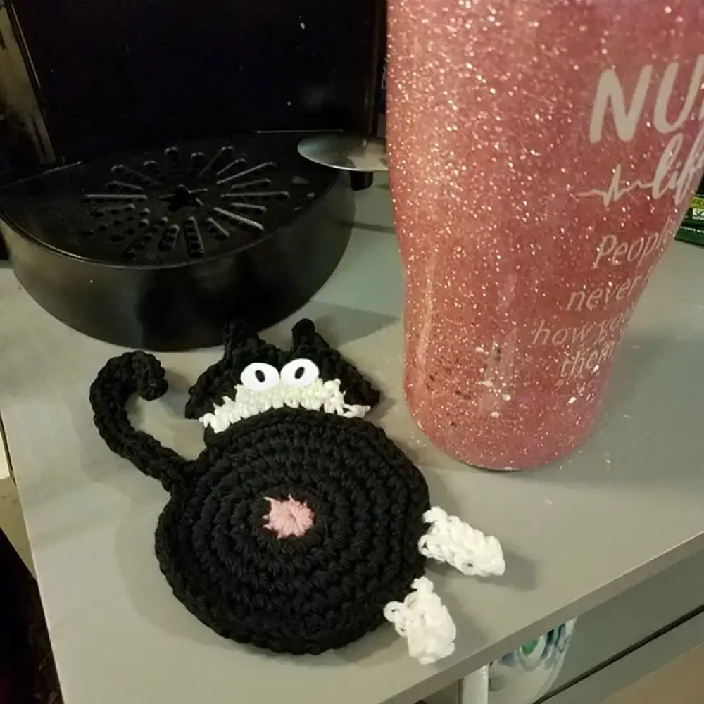 Handmade black crocheted cat butt coaster with white accents and pink nose from decorbites cat butt coasters set