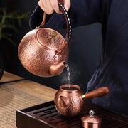 Handmade hammered copper tea pot with knitting handle and floral lid pouring steaming tea into matching copper pot decorbites handmade copper
