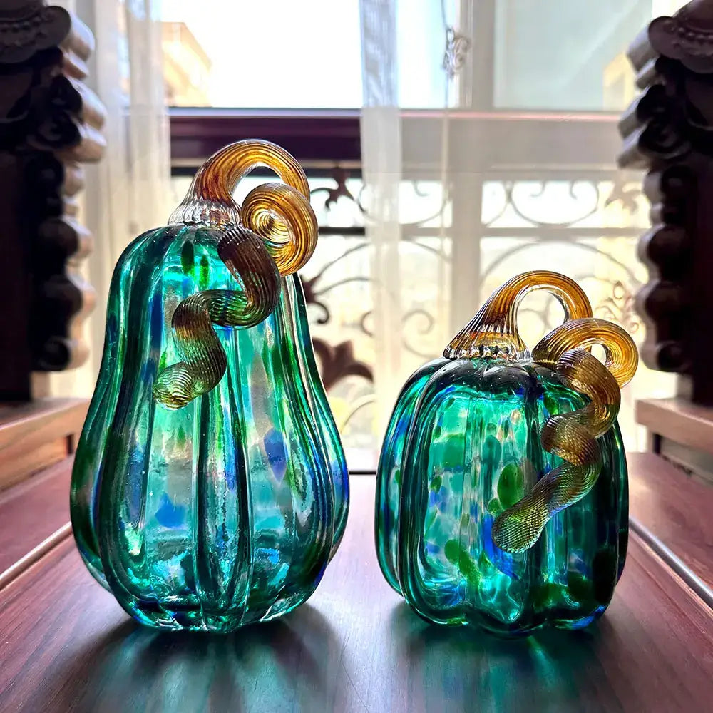 Two hand-blown glass pumpkin figurines in iridescent teal and green with amber-gold stems for living room decor