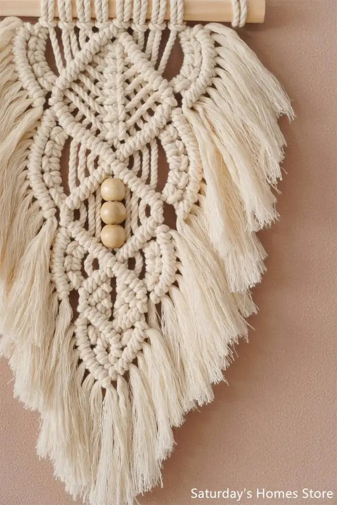 Cream-colored handmade macrame leaf wall hanging with wooden beads and fringe for olive green and off-white decor