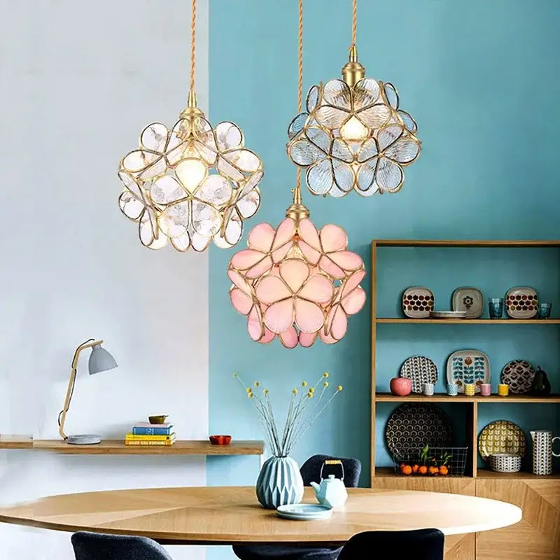 Three elegant flower-shaped glass petal pendant lights in pink and gold hang above a wooden dining table
