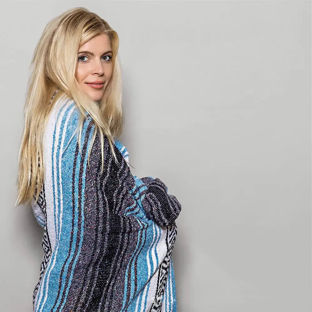 A woman draped in a decorbites handwoven mexican blanket with blue white black stripes and geometric patterns