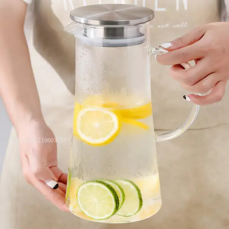 Clear glass pitcher water carafe with stainless steel lid and handle filled with lemon and lime slices in icy water