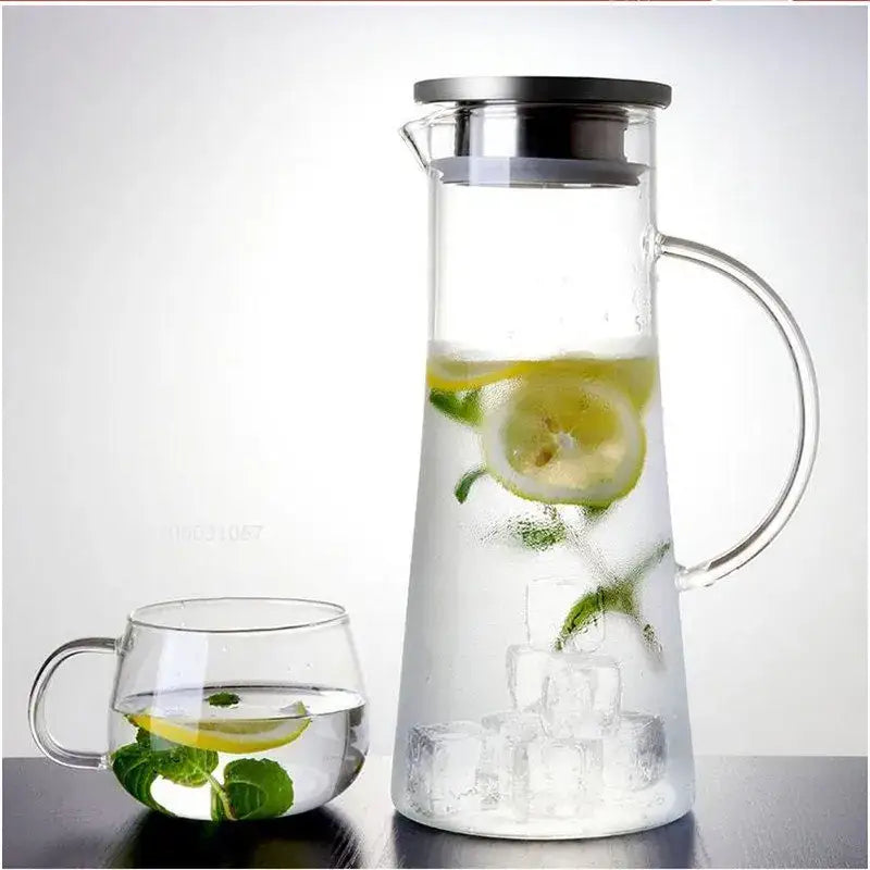 Heat resistant clear glass pitcher water carafe with stainless steel lid filled with ice water lemon and mint leaves