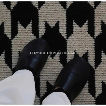 Black glossy leather clogs with rounded toe and low profile design placed on decorbites houndstooth black ivory area rug