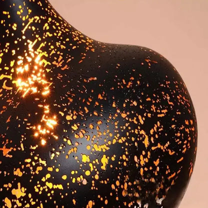 Black ceramic vase with glossy finish and gold splatters complementing decorbites etched wrought iron chandelier