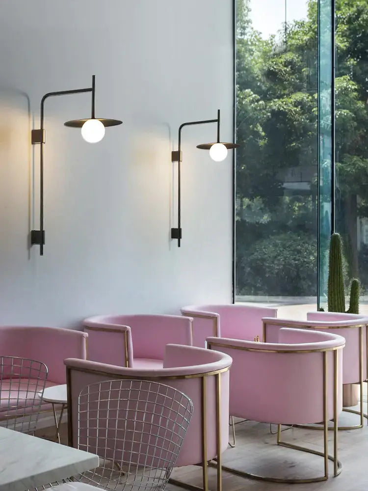 Pink upholstered armchairs with gold-toned metal frames next to an industrial black minimalist style wall lamp bedroom disc sconce
