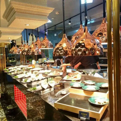 Copper industrial electric telescopic heat lamp pendant lights with ornate black and gold patterns hang above a buffet