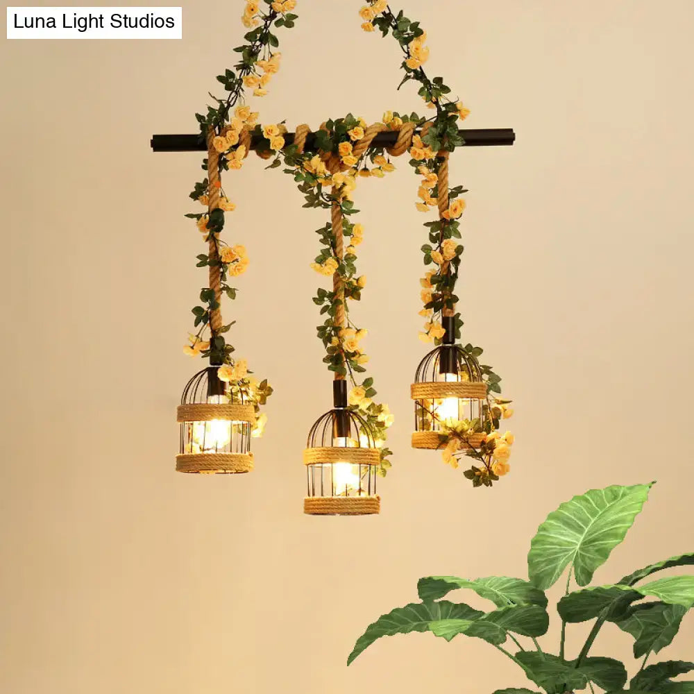 Three hanging black birdcage pendant lights with industrial hemp rope and yellow floral garlands for restaurant island lighting