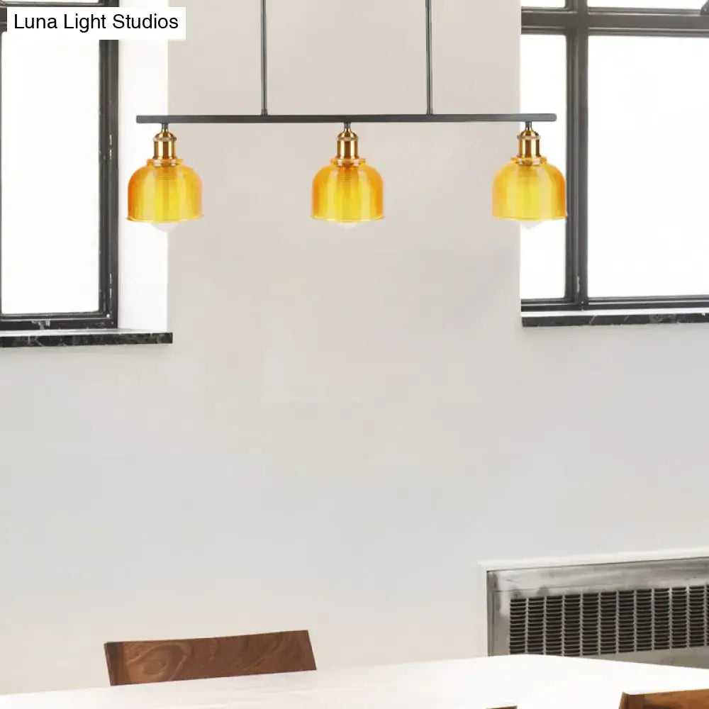 Set of three amber glass pendant lights with brass fixtures suspended from black metal bar for island lighting